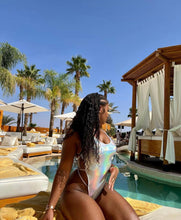 Load image into Gallery viewer, Woman in a swimsuit sitting by a pool with palm trees and lounge chairs in the background