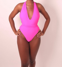 Load image into Gallery viewer, A model wearing a pink one-piece swimsuit with a deep V-neckline and broad shoulder straps.
