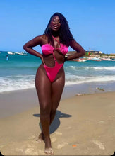 Load image into Gallery viewer, A woman standing on a beach wearing a pink one-piece swimsuit with a high-waisted design, posing with the ocean and beach in the background. shop this look at www.shaniika.com
