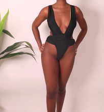 Load image into Gallery viewer, A female model wearing a black one-piece swimsuit with a deep V-neck cutout and high-thigh design.
